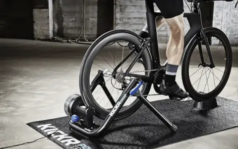 A person is engaged in indoor cycling training on a trainer in a gritty, industrial-style room.