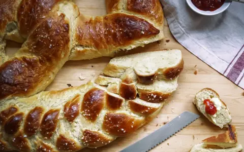 Goldbraune Neujahrsbrezel, mit Salz bestreut, auf einem Holztisch. Ein Stück ist mit Butter und Marmelade belegt. Ein tolles Neujahrsbrezel Rezept!