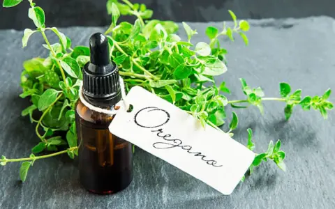 Frasco de aceite de orégano con ramitas frescas de la hierba. La etiqueta blanca dice "Oregano".