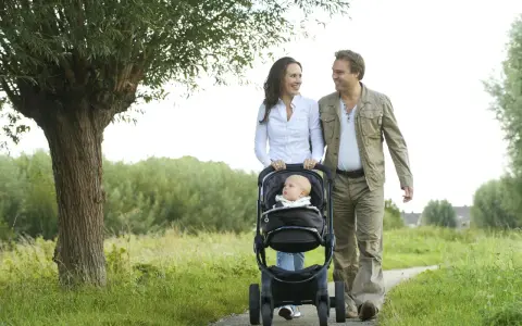 Szczęśliwi rodzice spacerują z dzieckiem w wózku, który można ustawić przodem i tylem do kierunku jazdy.