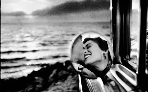 Un doux reflet dans le rétroviseur d'une voiture, une femme rit aux éclats, le regard tourné vers la mer.