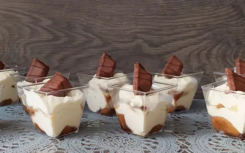 Słodkie deserki w pucharkach, przypominające tort Kinder Bueno, z kremem i kawałkami czekolady.