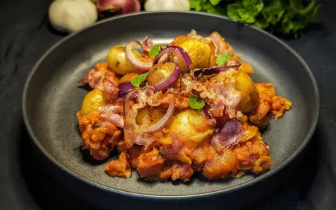 Herzhafte Salsiccia-Rezepte ohne Pasta: Kartoffeln, rote Zwiebeln und Speck in einer würzigen Tomatensauce, garniert mit frischen Kräutern.