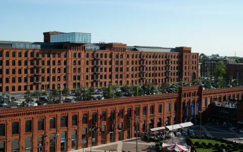 Dawna fabryka w Łodzi, dziś centrum handlowe i rozrywkowe. Widać tu architekturę z czerwonej cegły, parking, ogródki kawiarniane i karuzelę, tworząc ciekawe łódzkie atrakcje.