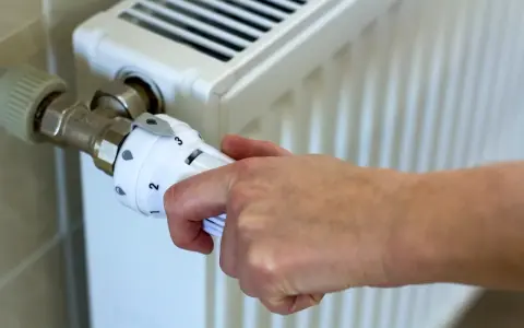 Dłoń reguluje termostat grzejnika. Kiedy zaczyna się sezon grzewczy? Zazwyczaj od października do kwietnia.