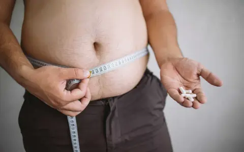 En person mäter sin midja med ett måttband, håller piller i handen. Kan indikera hormonell obalans och viktuppgång.