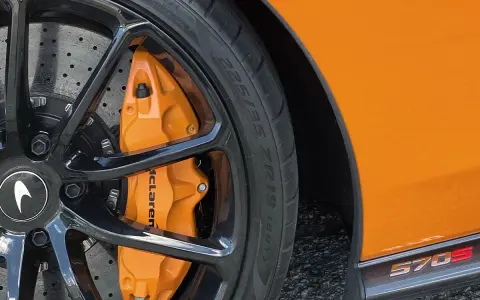 Pomarańczowy zacisk hamulcowy McLaren na czarnym, wieloramiennym kole. Opona z napisem 225/35 ZR19.