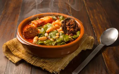 Un humeante pote asturiano, con fabes, berzas, chorizo y tocino, servido en cazuela de barro sobre arpillera.