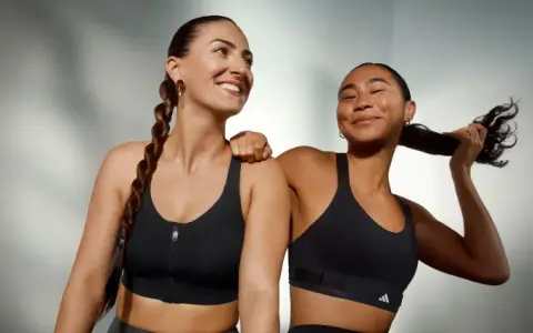 Two women in black sports bras, one with a braid, the other playing with her hair.