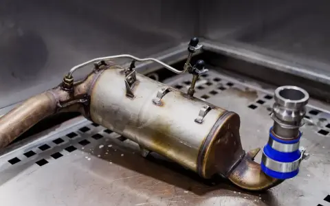 Element układu wydechowego diesla, potencjalnie z objawami zapchanego EGR. Widoczny metalowy cylinder z rurkami i zaciskami.