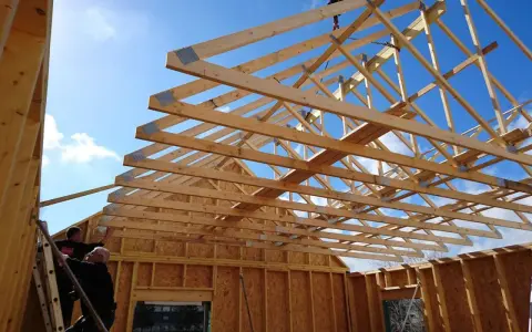 Construction d'une charpente fermette en bois sous un ciel bleu. Des ouvriers travaillent sur l'installation.