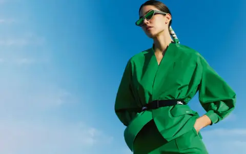 Une femme en tenue verte éclatante, lunettes de soleil futuristes, pose sous un ciel bleu. Un **cahier de tendance** inspirant.