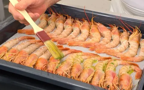 Un pincel baña con aceite y hierbas unos gambones al horno listos para cocinar.
