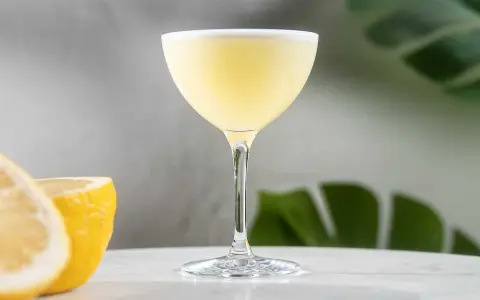 En elegant lemon martini med en lätt skumkrona, serverad med färska citronklyftor i bakgrunden.
