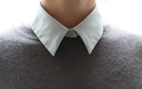 Gros plan sur un col froncé blanc sur un pull gris.