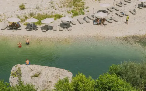 Wczasy w Albanii: ludzie odpoczywają na plaży nad krystalicznie czystą wodą, niektórzy kąpią się, inni relaksują pod parasolami.