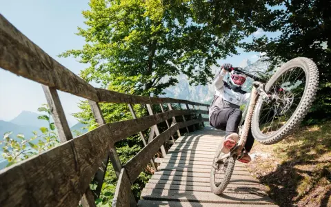 Ciclista in azione durante il giro del lago di Molveno in bici, su un ponte di legno tra alberi verdi e montagne.