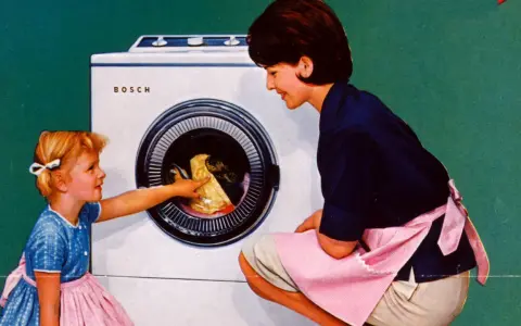 Mutter und Kind vor der ersten Waschmaschine. Das kleine Mädchen hilft beim Einräumen der Wäsche.