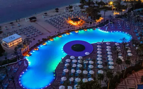 Luksusowy basen z niebieskim podświetleniem i leżakami na plaży w Dubaju.