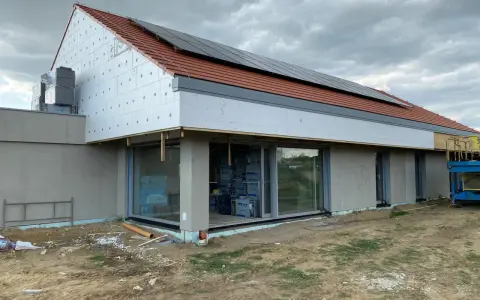 Budowa domu z dachówką i panelami słonecznymi. Dach bezokapowy z widoczną izolacją styropianową i oknami.