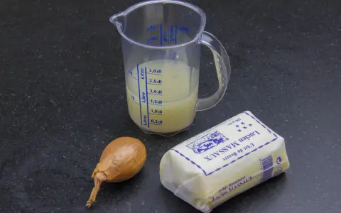 Ingrédients pour un beurre blanc : un oignon, un pichet gradué avec du liquide, et un beau morceau de beurre Lucien Massaux.