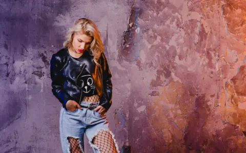 Blondynka w skórzanej kurtce i podartych dżinsach, z siatką na nogach, emanuje **grunge**'owym klimatem.