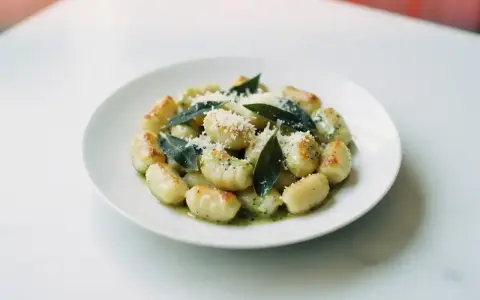 Pyszne gnocchi z sosem, posypane parmezanem i ozdobione listkami szałwii. Idealne danie dla miłośników włoskiej kuchni.
