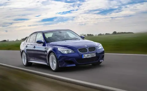 Niebieskie BMW M5 E60, ikona designu Chrisa Bangle'a, pędzi po drodze wśród zielonych pól i błękitnego nieba.