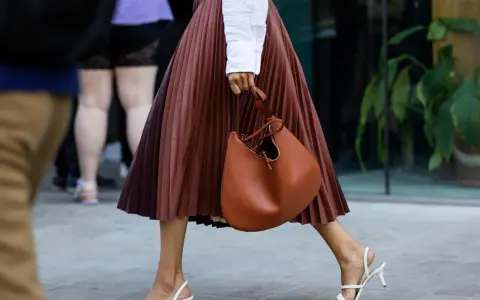 Elegant brauner Faltenrock, kombiniert mit weißer Bluse und cognacfarbener Tasche. Ein stilvoller Look für den Sommer.