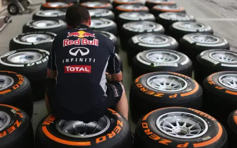 Mechanik w stroju Red Bulla siedzi wśród rzędów opon F1.