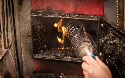 Ręka wrzuca plastikową butelkę do pieca. To może być mandat za palenie śmieci na podwórku.