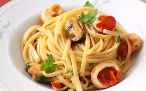 Tallarines con gambas al ajillo, mejillones y calamares, salpicados con perejil fresco y trocitos de tomate.