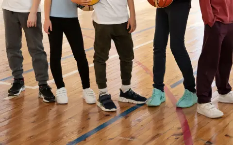Dzieci na sali gimnastycznej, zastanawiające się, jakie buty na WF do szkoły wybrać. Różne modele sportowego obuwia na drewnianej podłodze.