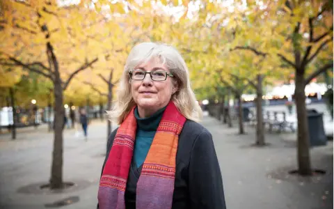 Kvinna med glasögon och färgglad scarf i höstpark. Hon verkar inte ha ont i leder brist på energi, utan njuter av den vackra naturen.