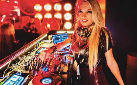 Une dj femme connue aux platines, mixant dans une ambiance club avec des lumières rouges.