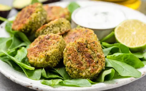 Polpette di spinaci dorate su un letto di spinaci freschi, con una ciotolina di salsa e spicchi di lime.