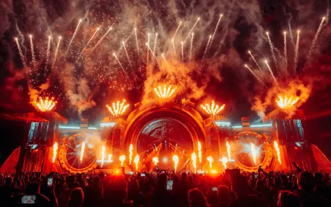 Spektakularny pokaz fajerwerków i płomieni na scenie podczas festiwalu Sunrise Festival 2026. Tłum ludzi z telefonami wzniesionymi ku górze.