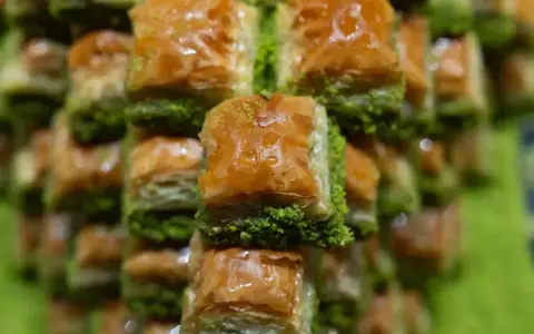 Słodka, złocista baklava, co to za przysmak! Warstwy ciasta filo, orzechów i syropu, posypane zielonymi pistacjami.