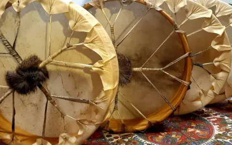 Trois tambours chamaniques, un instrument traditionnel aux peaux tendues et ornées de franges, prêts pour une cérémonie.