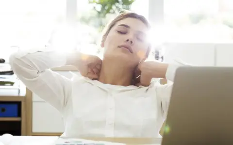 Zmęczona kobieta przy biurku masuje kark. Może potrzebuje czegoś na ból, np. Xefo Rapid na co?