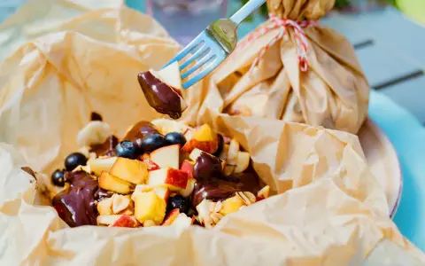 Fruchtiger Nachtisch vom Grill: Apfelstücke, Blaubeeren und Bananen mit Schokoladensauce, serviert in Papier.