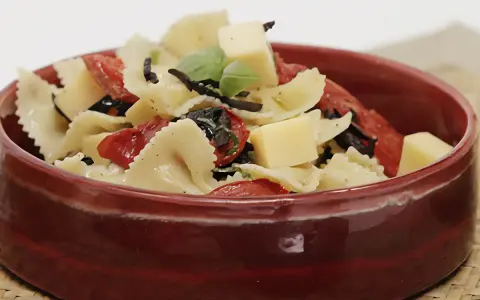 Deliciosa pasta farfalle con tomates secos, aceitunas negras, albahaca y cubos de queso. Una de las mejores recetas de pasta para disfrutar.
