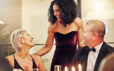 Drei Personen in eleganter Galadinner Kleidung lachen und unterhalten sich bei Kerzenlicht.