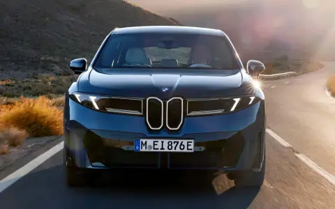 Der BMW iX4 fährt auf einer kurvigen Straße durch eine bergige Landschaft im goldenen Licht der Abendsonne.