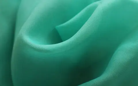 Detaljerad bild av turkos polyestertyg som visar hur tillverkas polyester genom vävning.
