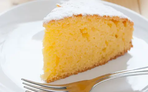 Ein saftiges Stück vanille kuchen, bestäubt mit Puderzucker, wartet auf einer weißen Platte mit einer Gabel.