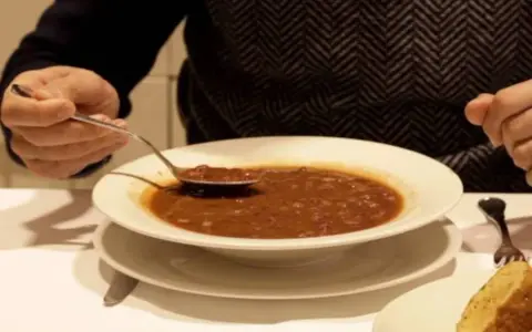 Persona prueba una cucharada de una humeante olla podrida, un plato reconfortante y tradicional.