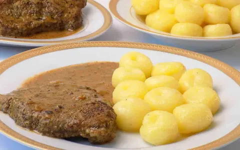 Pyszna karkówka w sosie, podana z kluskami śląskimi. Danie wygląda apetycznie i zachęca do spróbowania.