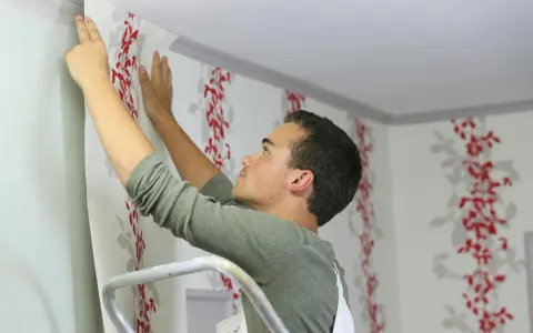 Mann tapeziert mit roter Blumenmuster-Tapete die Decke.