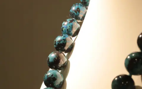 Collana di sfere in crisocolla pietra, con sfumature blu e nere, su sfondo chiaro e scuro.